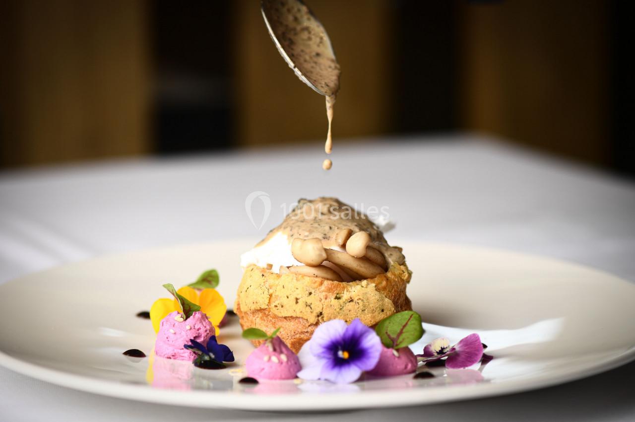Un plat raffiné avec une sauce versée sur un soufflé garni de champignons, accompagné de fleurs comestibles.
