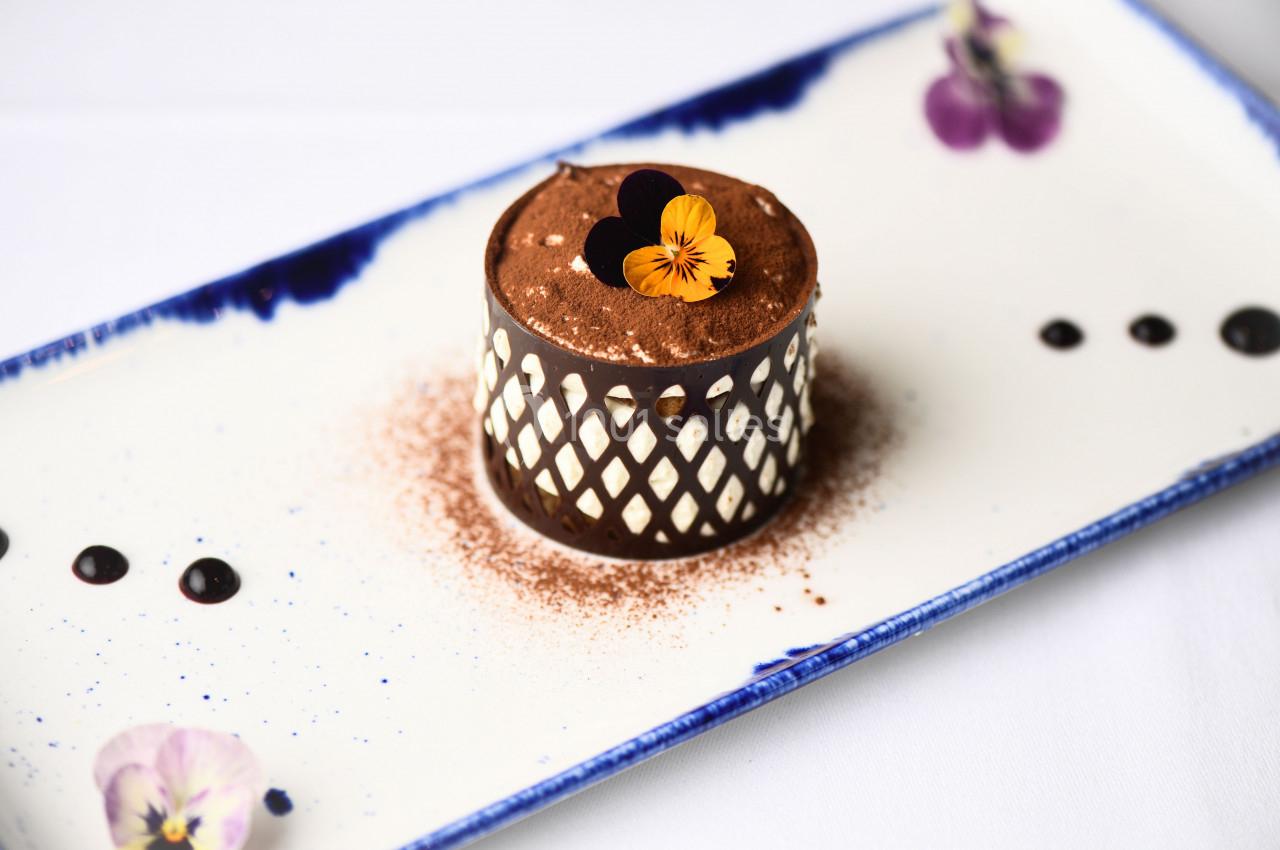 Dessert au chocolat décoré de fleurs comestibles sur une assiette blanche ornée de motifs floraux.
