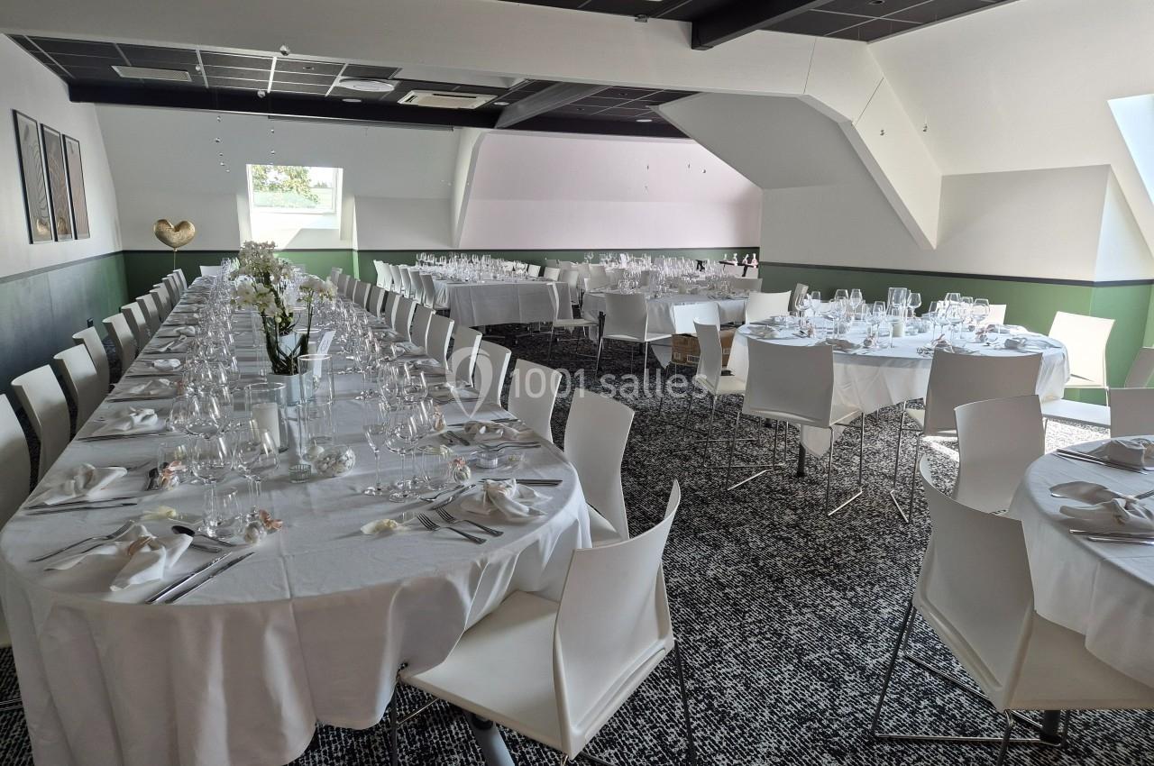 Salle de réception lumineuse avec tables dressées en blanc, chaises modernes et décoration sobre.