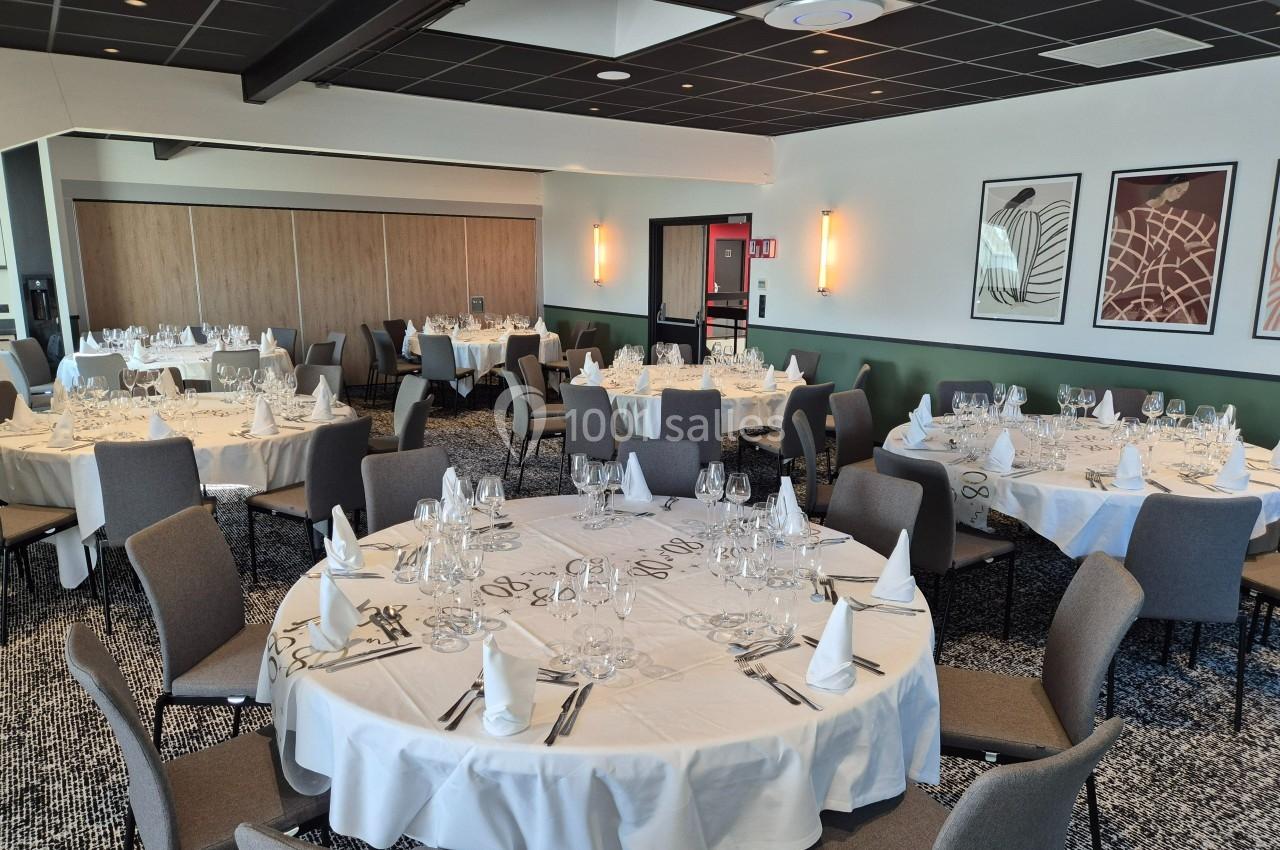 Salle de restaurant avec tables rondes dressées, nappes blanches, serviettes pliées et verres disposés.