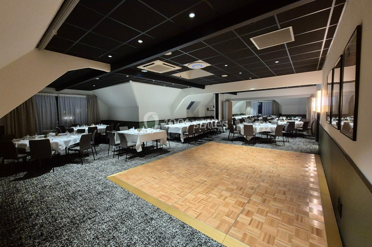 Salle de réception avec tables dressées, chaises alignées et piste de danse en bois au centre.