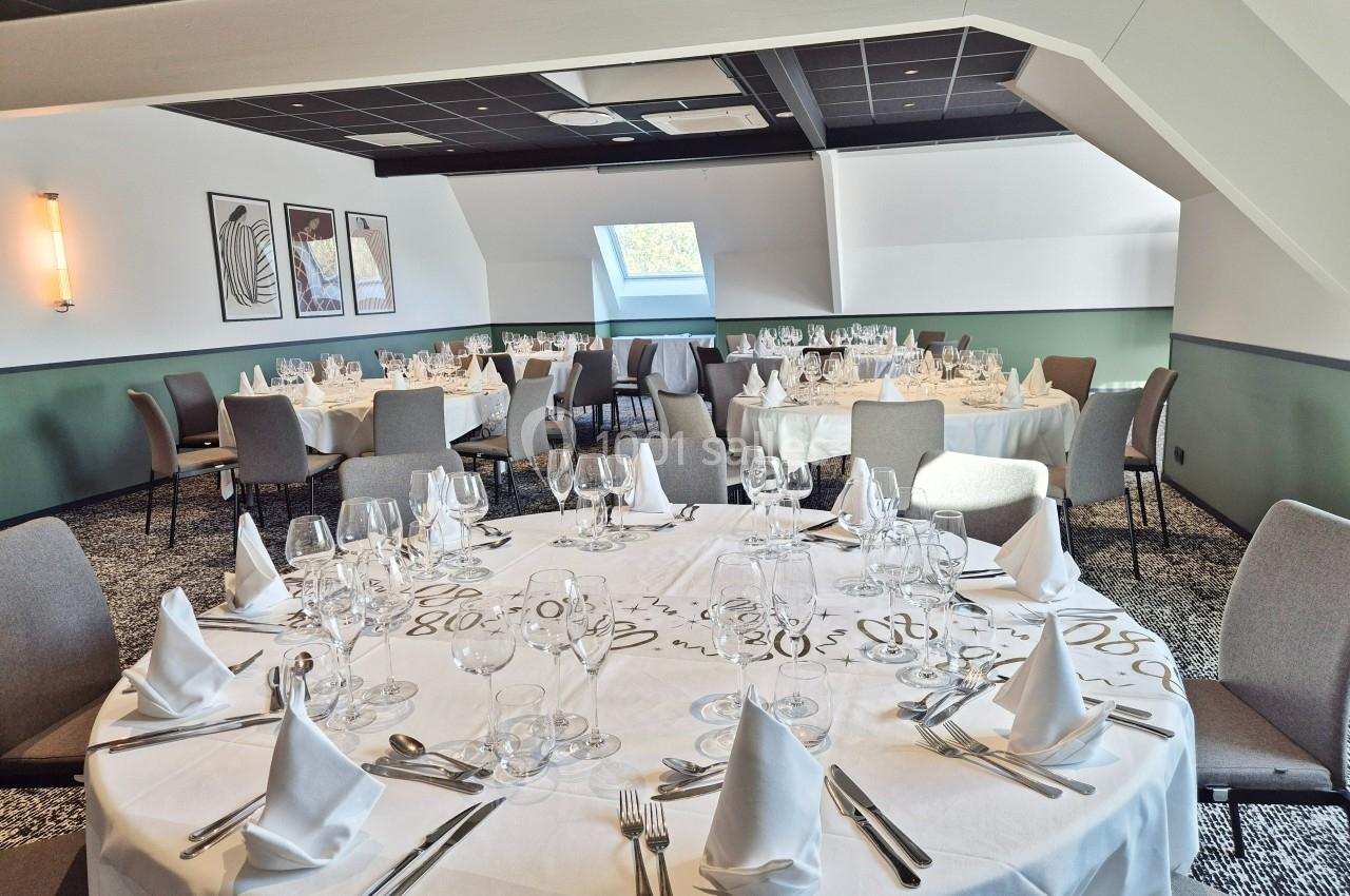 Salle de réception lumineuse avec tables rondes dressées, nappes blanches et chaises grises.