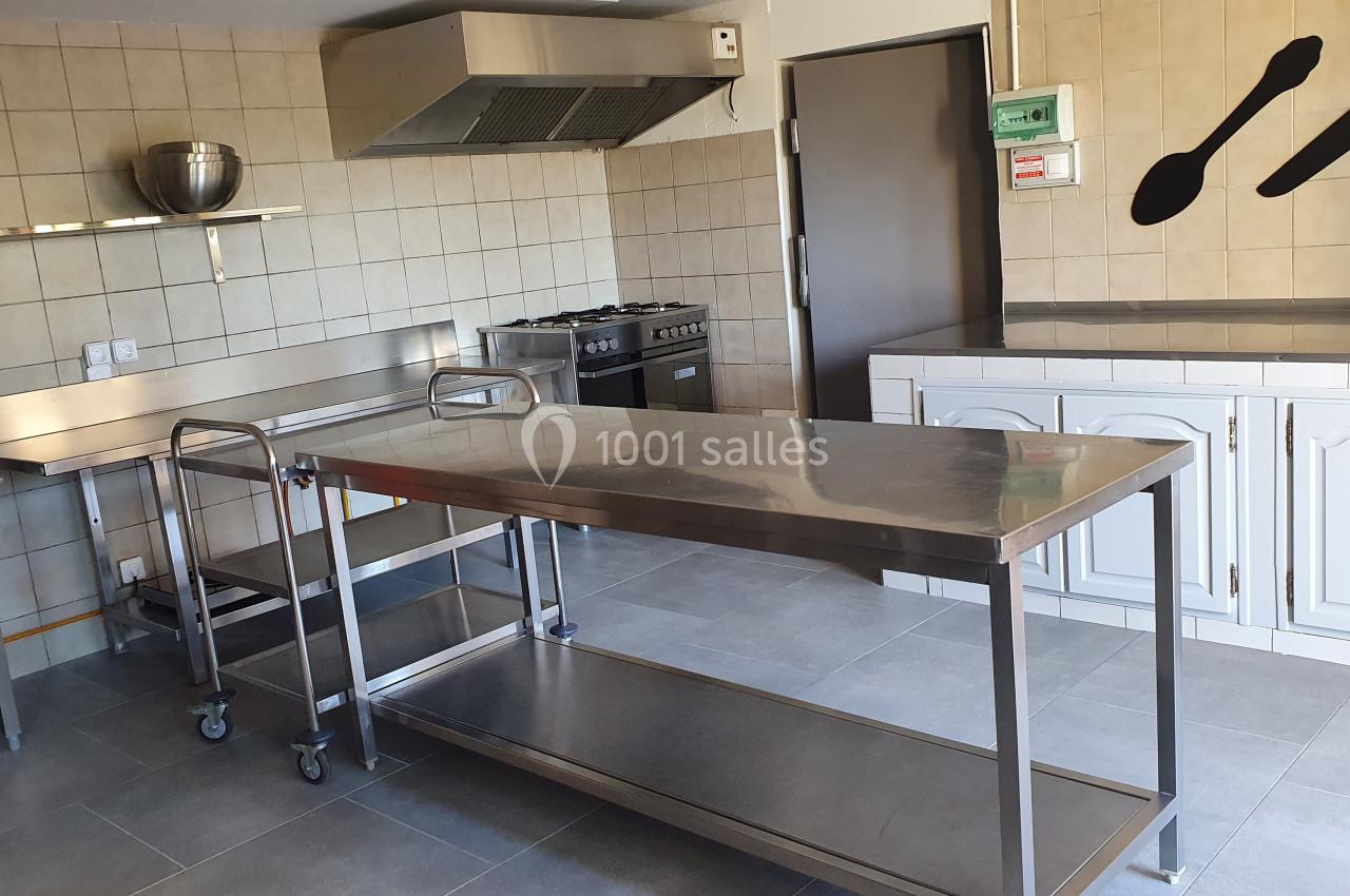 Cuisine professionnelle avec plans de travail en inox, étagères murales, cuisinière et carrelage beige au mur.