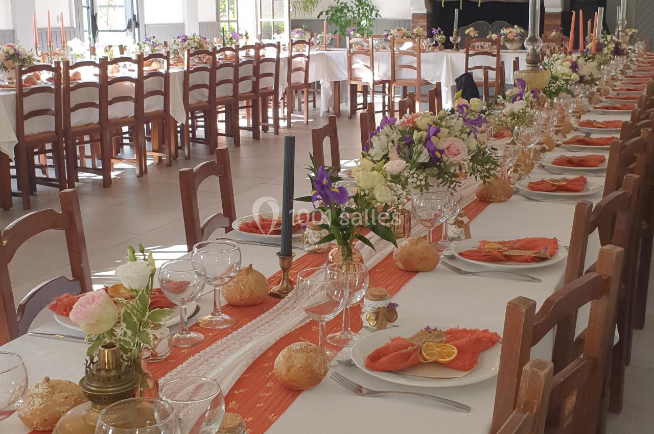 Salle de réception décorée avec des tables dressées, nappes blanches, fleurs et assiettes garnies de saumon fumé.