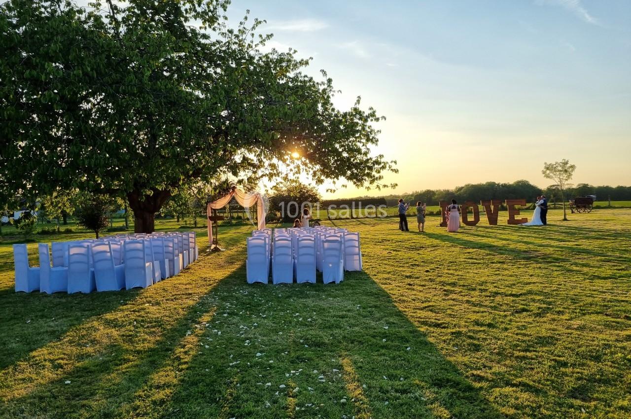 Chaises alignées sous un arbre pour une cérémonie en plein air au coucher du soleil, avec des lettres géantes ’LOVE’ en…