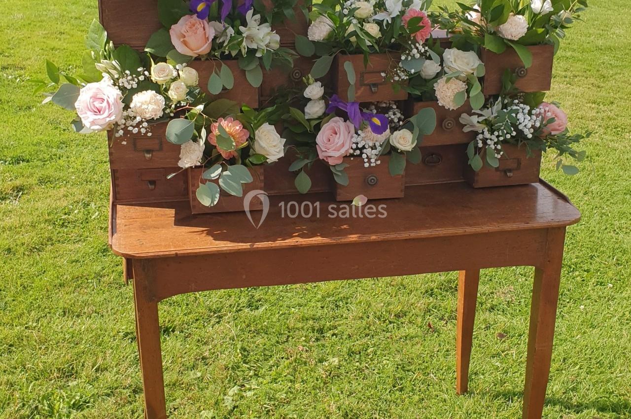 Arrangement floral dans des tiroirs en bois empilés sur une table en bois, posé sur une pelouse sous un ciel dégagé.