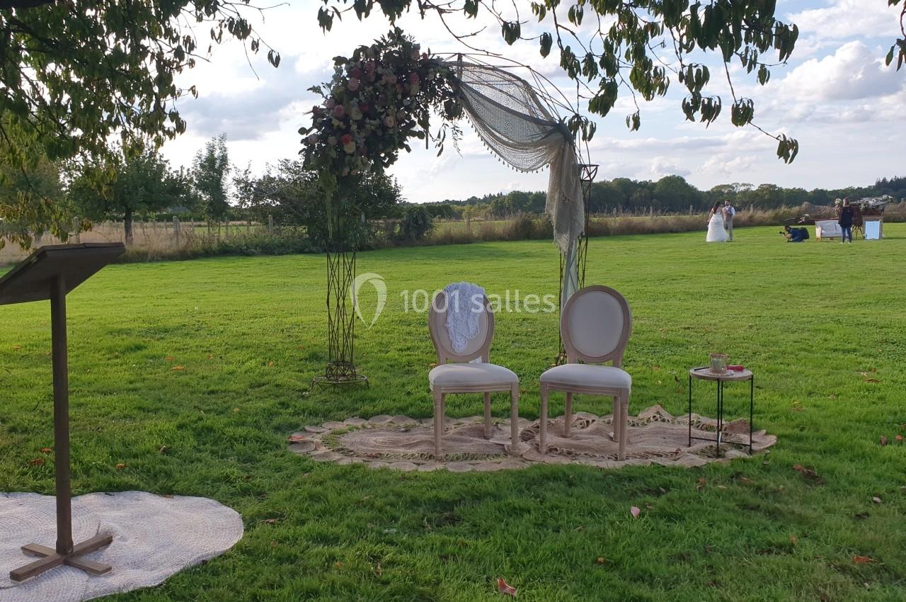 Deux chaises décorées sous une arche florale dans un jardin, préparées pour une cérémonie en plein air.
