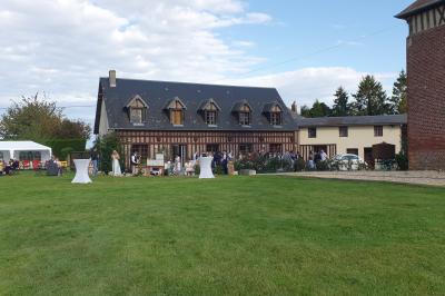 Bâtiments en colombages et en briques avec toiture en ardoise, entourés de végétation sous un ciel partiellement nuageux.