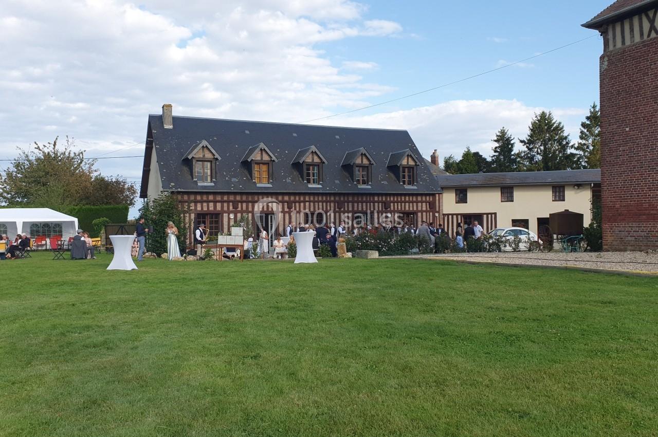 Grande maison à colombages avec jardin, tables hautes et invités rassemblés pour un événement en plein air.