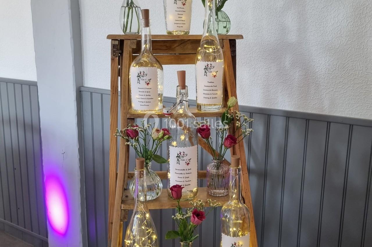 Échelle en bois décorée de bouteilles lumineuses et de petits bouquets de fleurs rouges et jaunes.