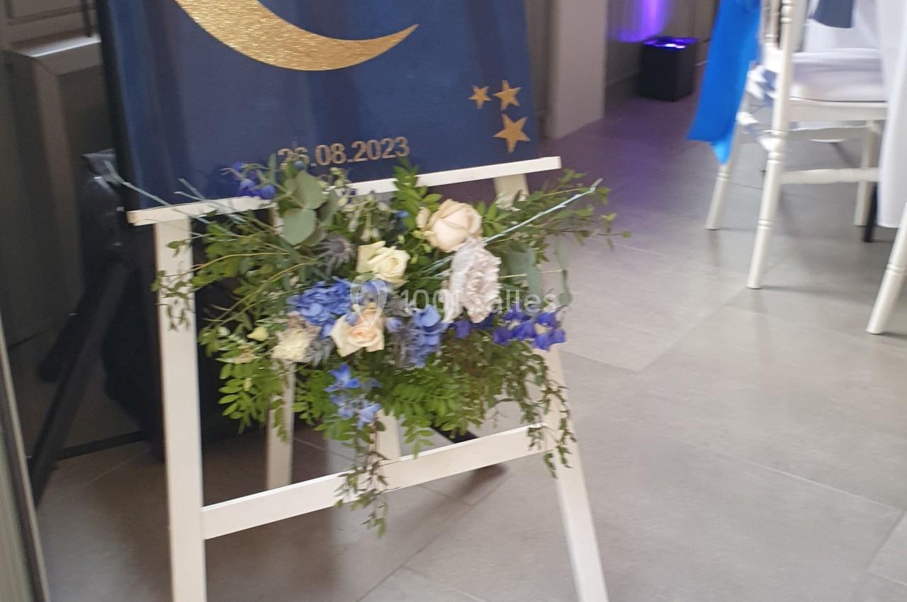 Panneau de bienvenue avec des noms et une date, décoré de fleurs bleues et blanches, placé sur un chevalet.
