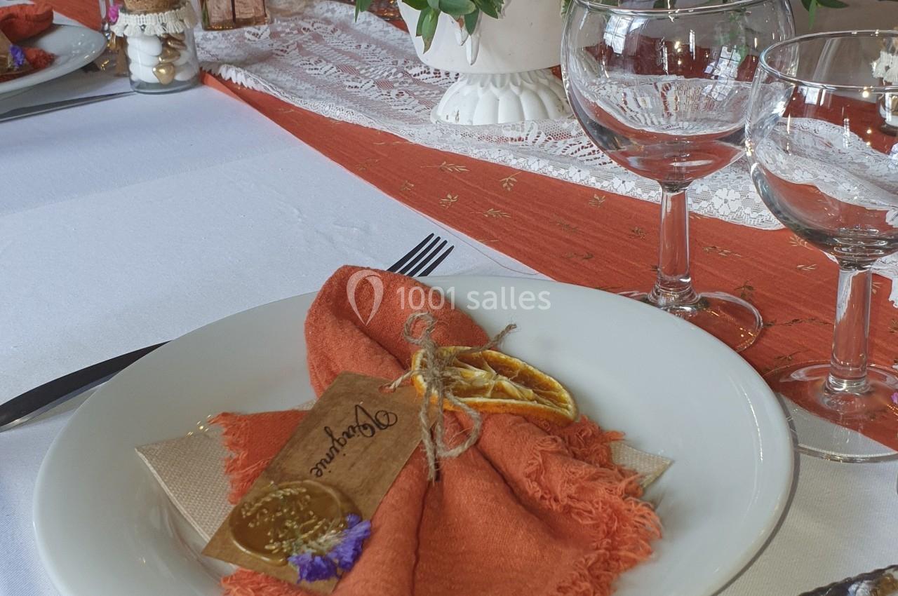 Table dressée avec une assiette blanche, une serviette orange décorée d'un brin de lavande et un centre de table fleuri.
