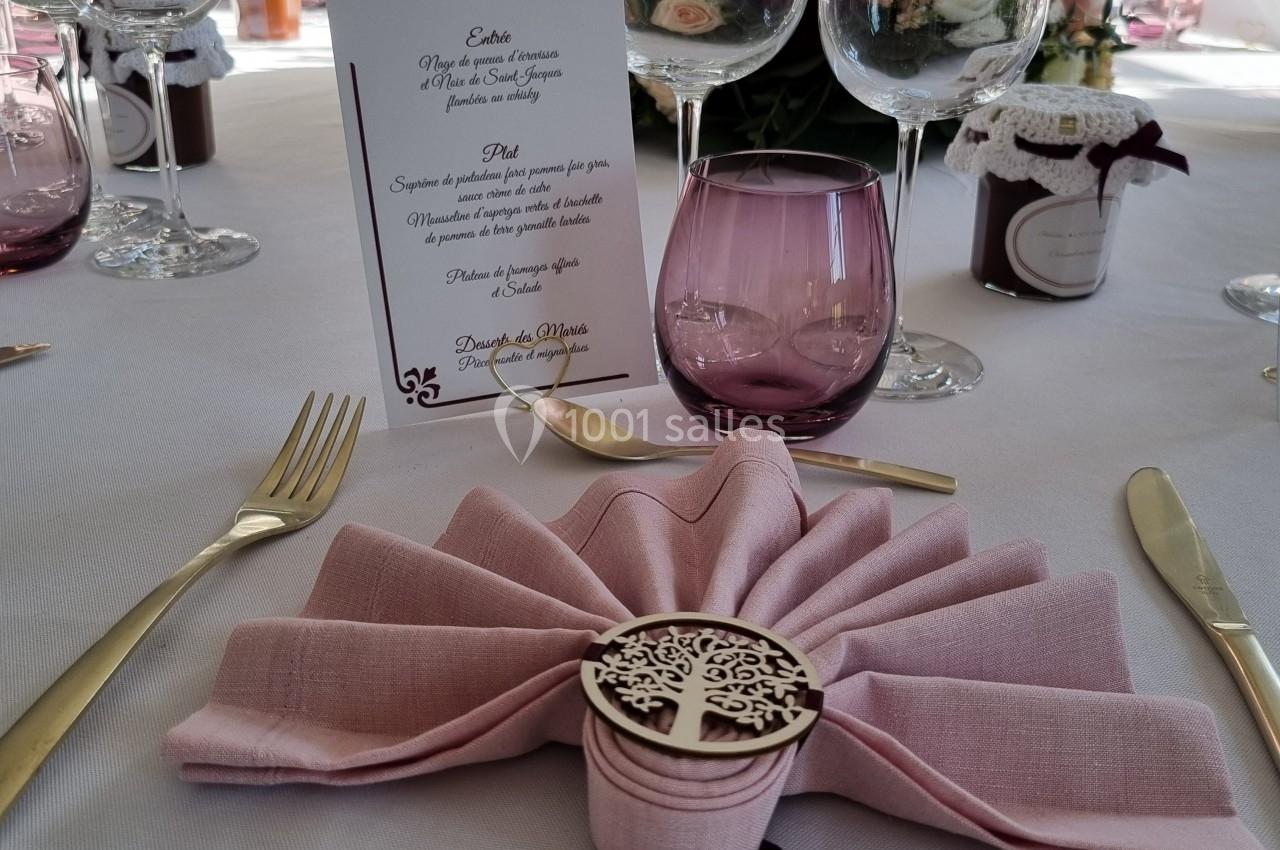 Table de réception élégamment dressée avec serviette pliée, menu, verres et décorations florales.