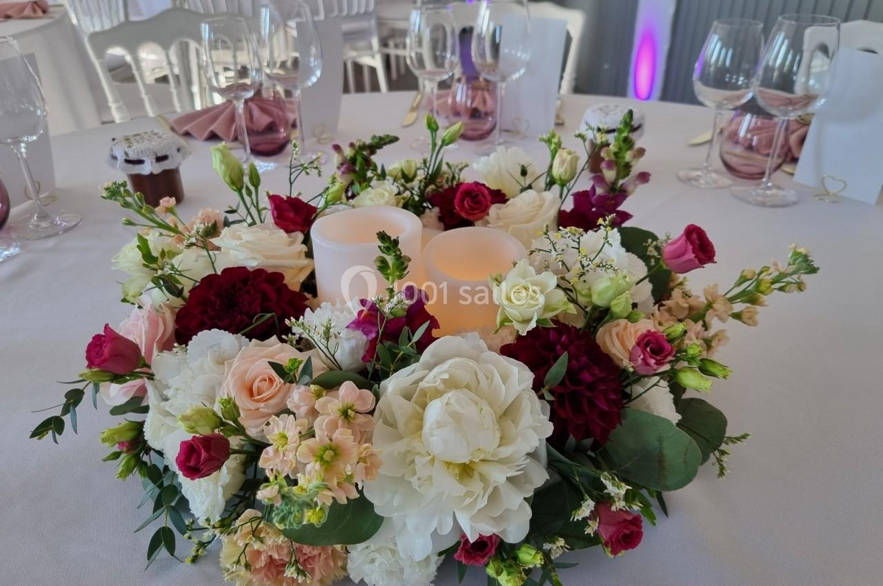 Centre de table floral avec bougies LED entourées de roses, pivoines et feuillage, sur une nappe blanche.