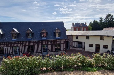 Bâtiments en colombages et en briques avec toiture en ardoise, entourés de végétation sous un ciel partiellement nuageux.