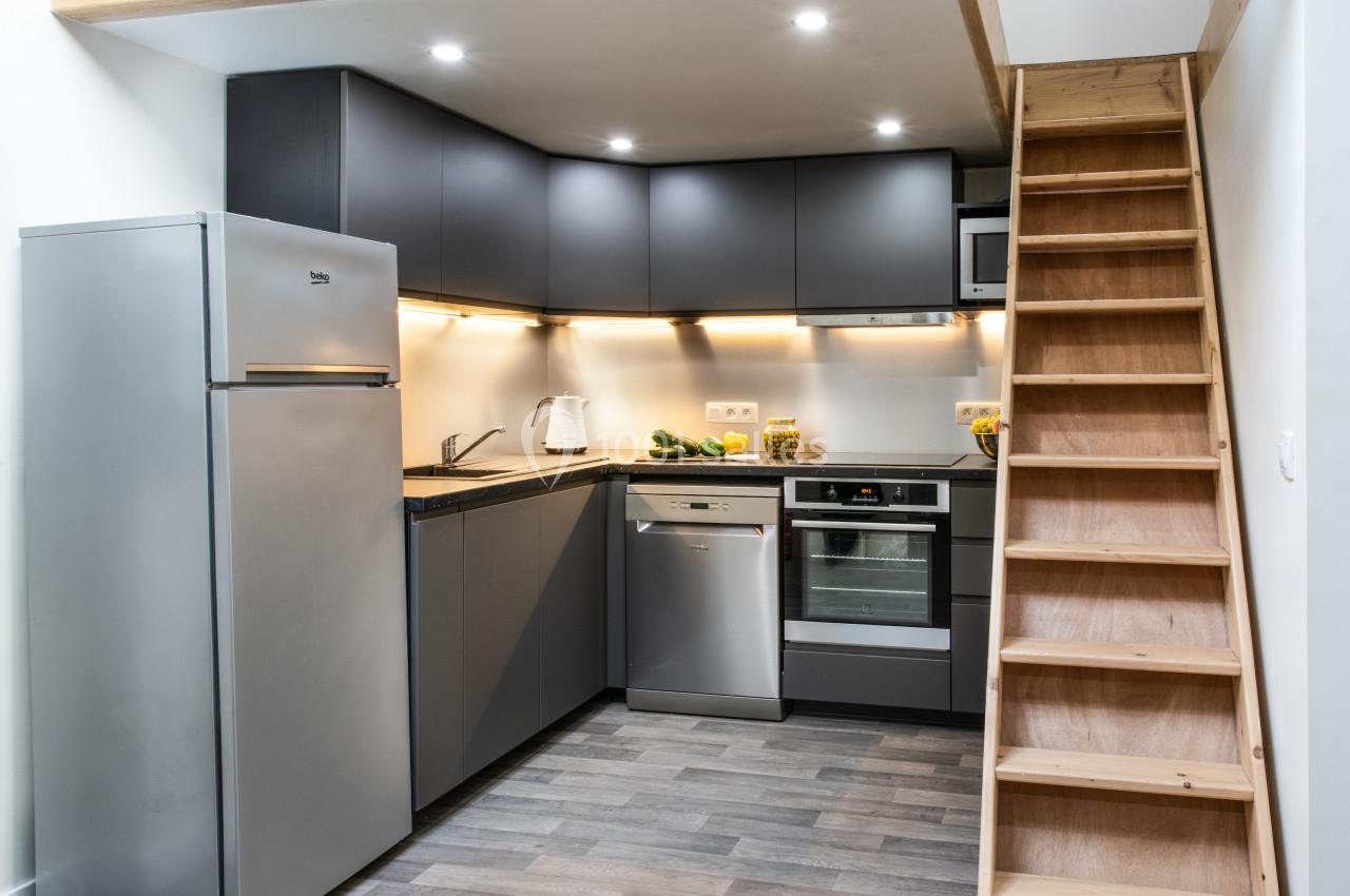 Cuisine moderne avec meubles gris, électroménagers en acier inoxydable et escalier en bois adjacent.