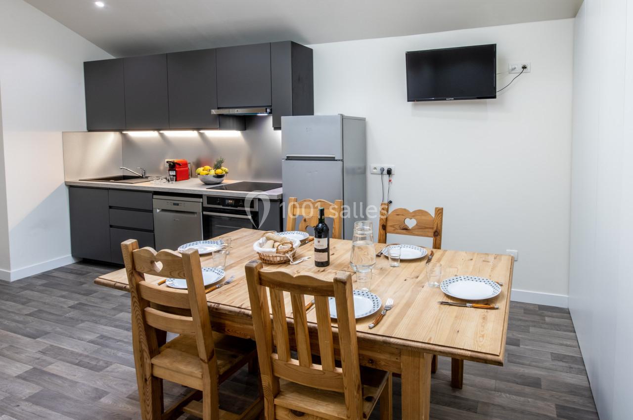 Cuisine moderne avec table en bois dressée pour quatre personnes, équipée d'appareils électroménagers et d'une télévision…
