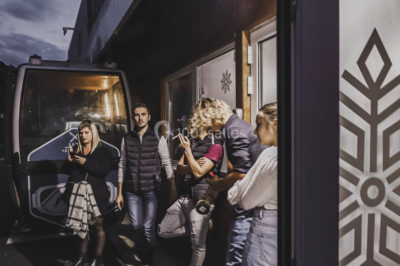 Un groupe de personnes discute devant un bâtiment et une cabine de téléphérique, en soirée.