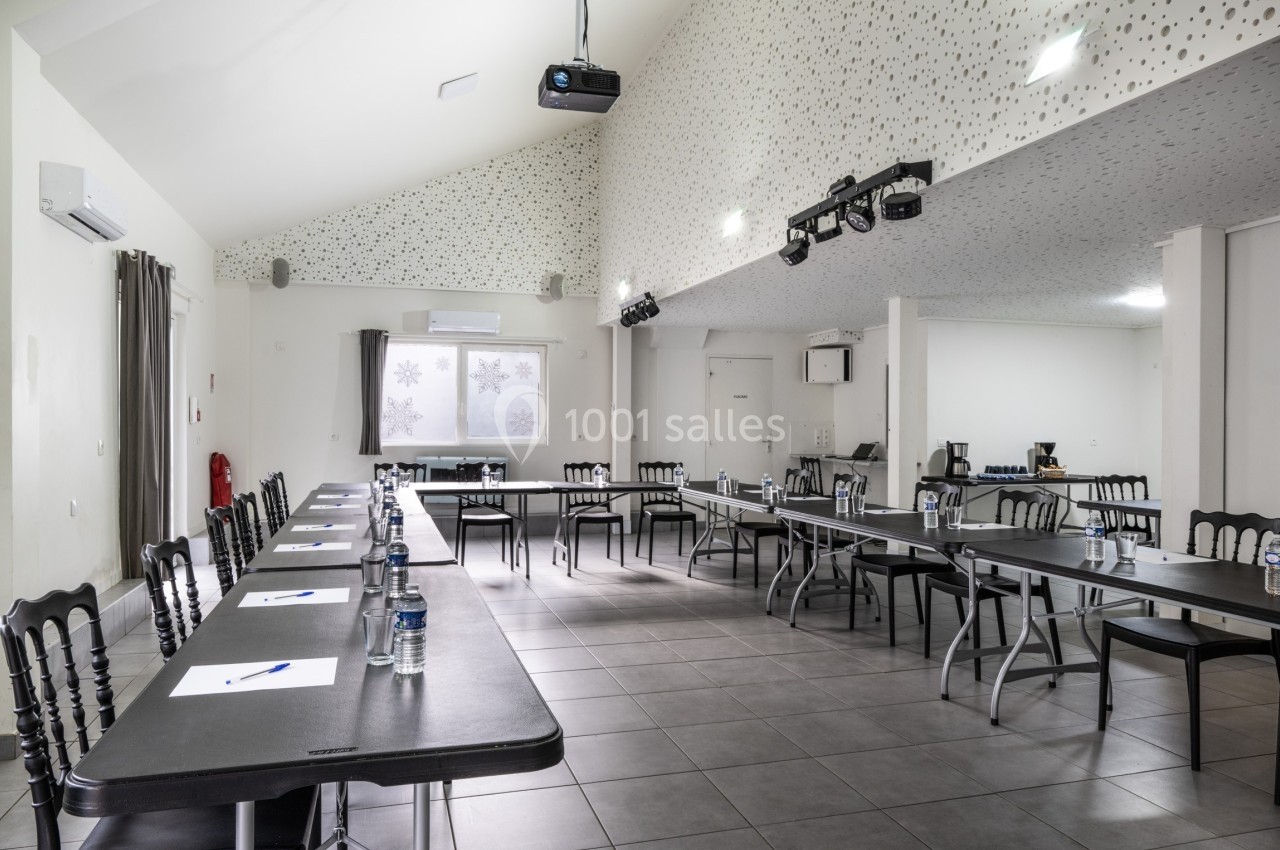 Salle de réunion lumineuse avec tables disposées en U, chaises noires, bouteilles d'eau et matériel de présentation.