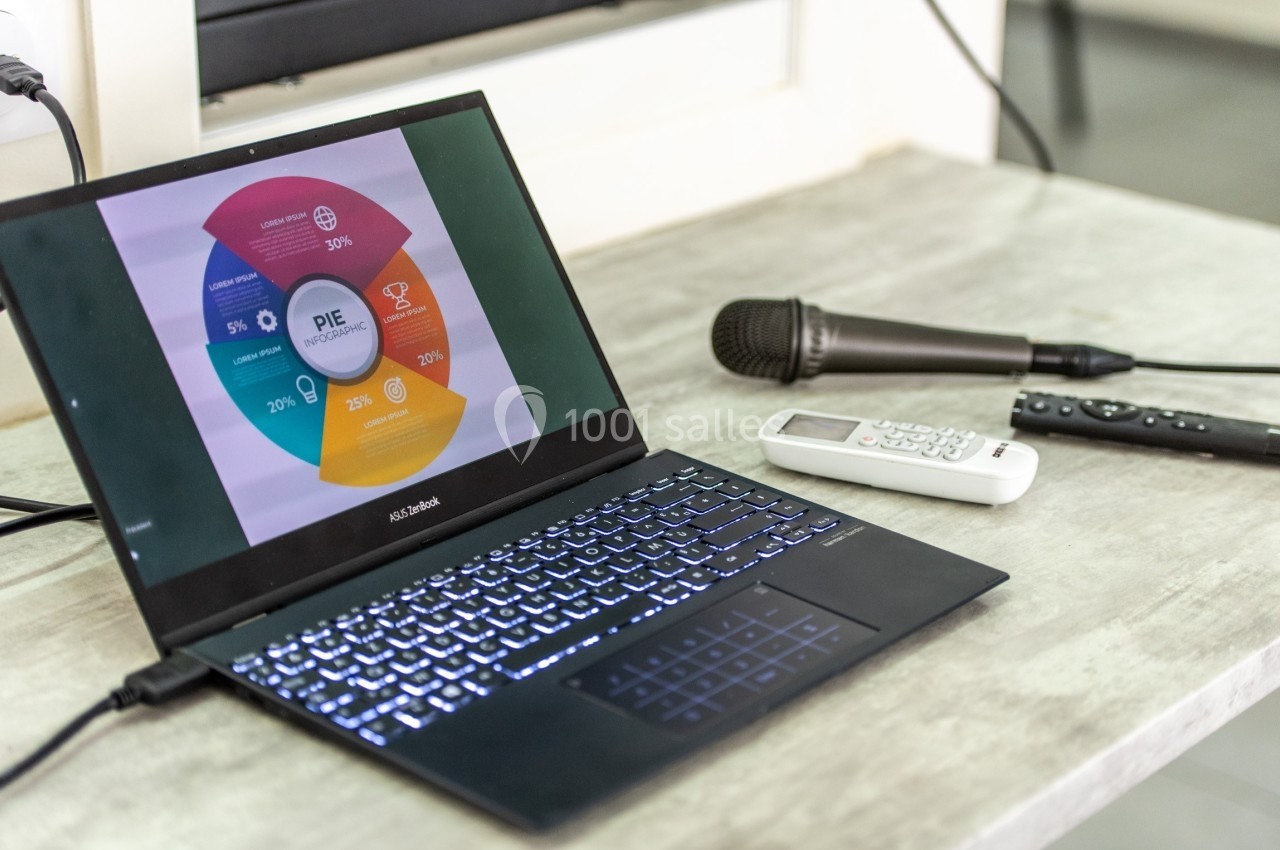 Ordinateur portable affichant un graphique circulaire coloré, posé sur une table avec un microphone et une télécommande.