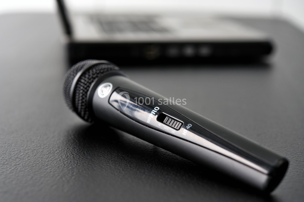 Microphone noir posé sur une table noire, avec un ordinateur portable flou en arrière-plan.