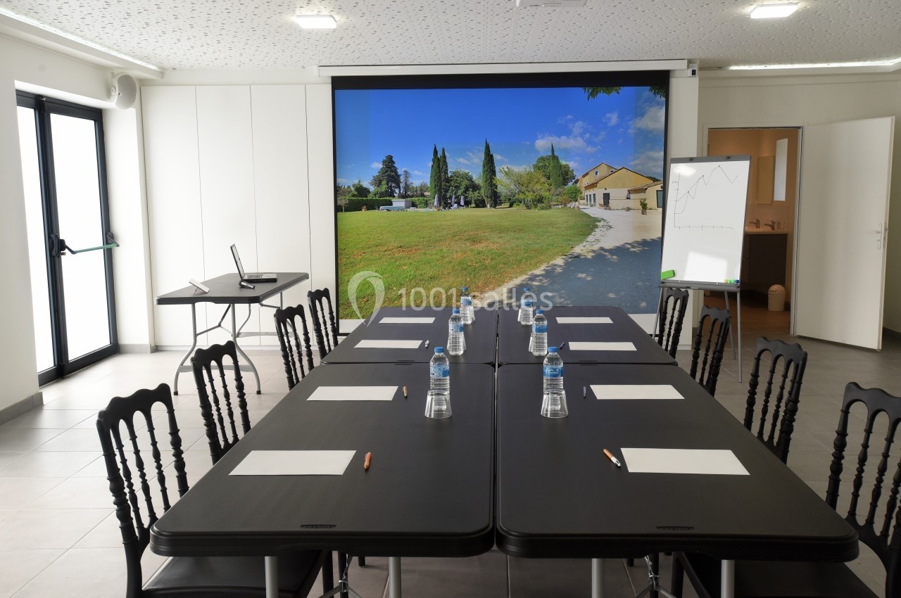 Salle de réunion lumineuse avec une grande table, des chaises, des documents, et un écran affichant un paysage extérieur.