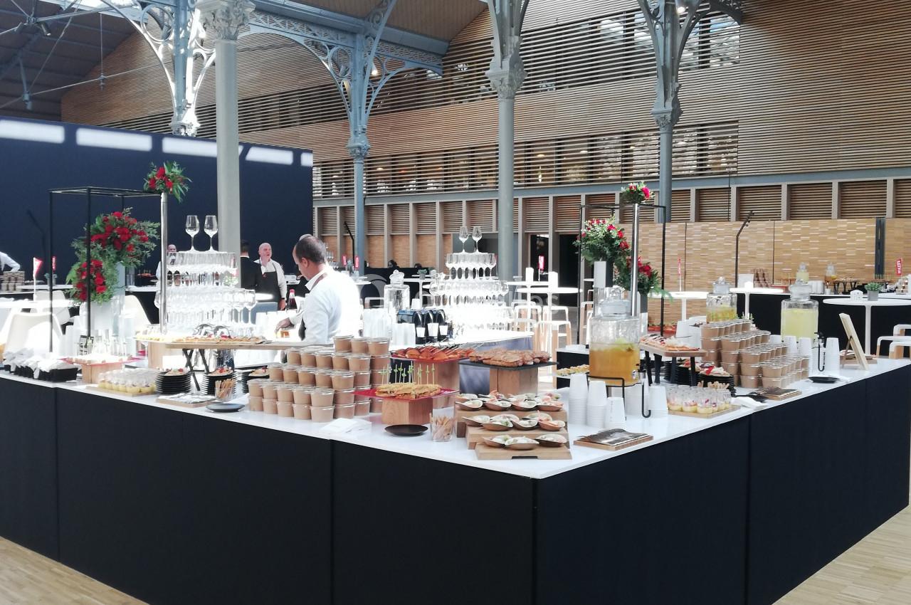 Buffet dressé dans une grande salle avec structure métallique, proposant boissons, viennoiseries et plats variés.