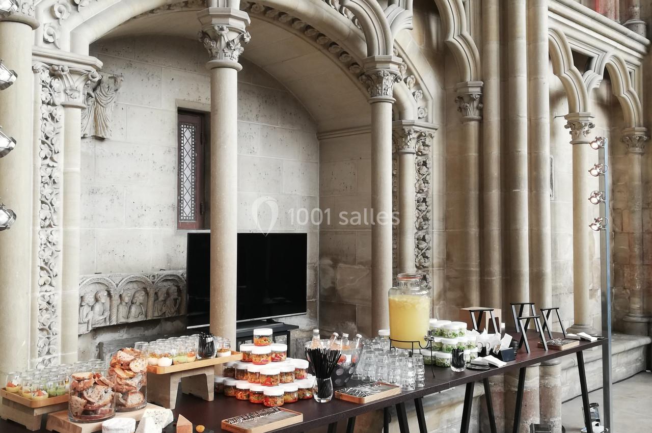 Buffet disposé sur des tables dans un espace architectural avec arches en pierre et vitraux en arrière-plan.