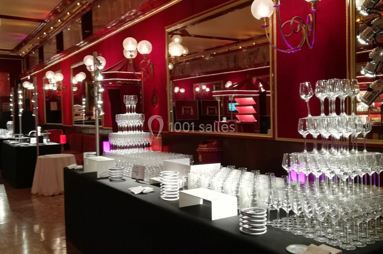 Salle élégante avec tables noires garnies de verres en cristal, éclairage chaleureux et décorations rouges et dorées.