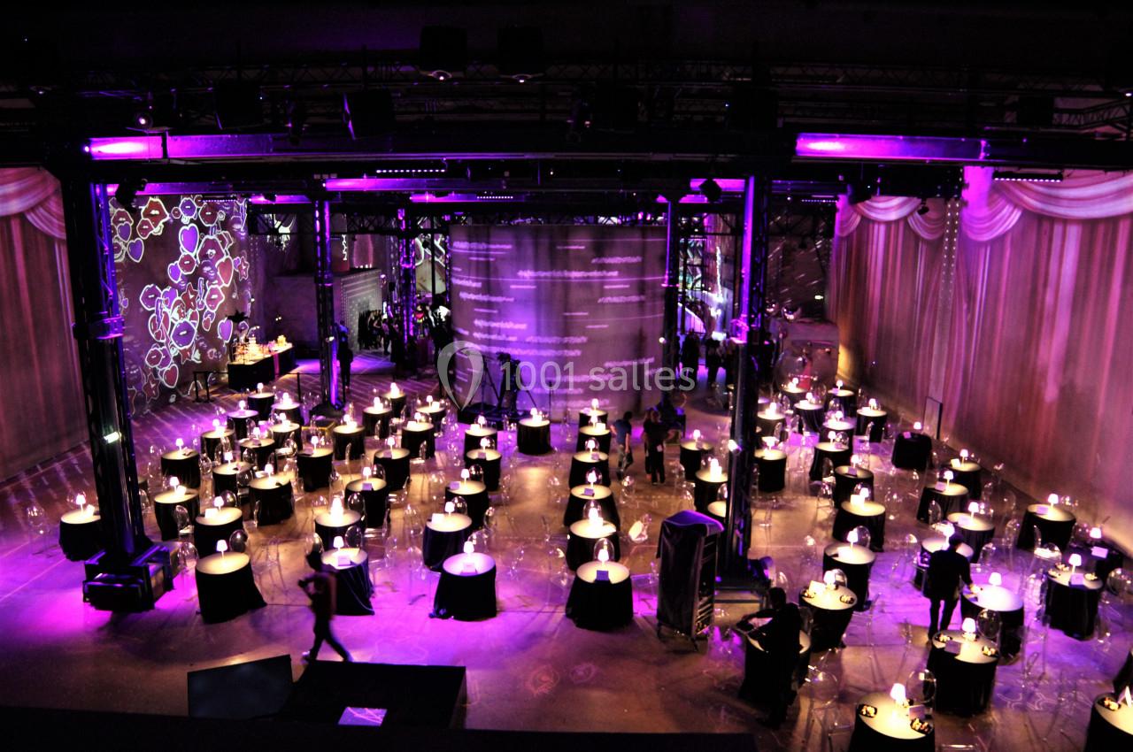 Salle de réception décorée avec des tables rondes éclairées par des bougies, ambiance lumineuse violette.