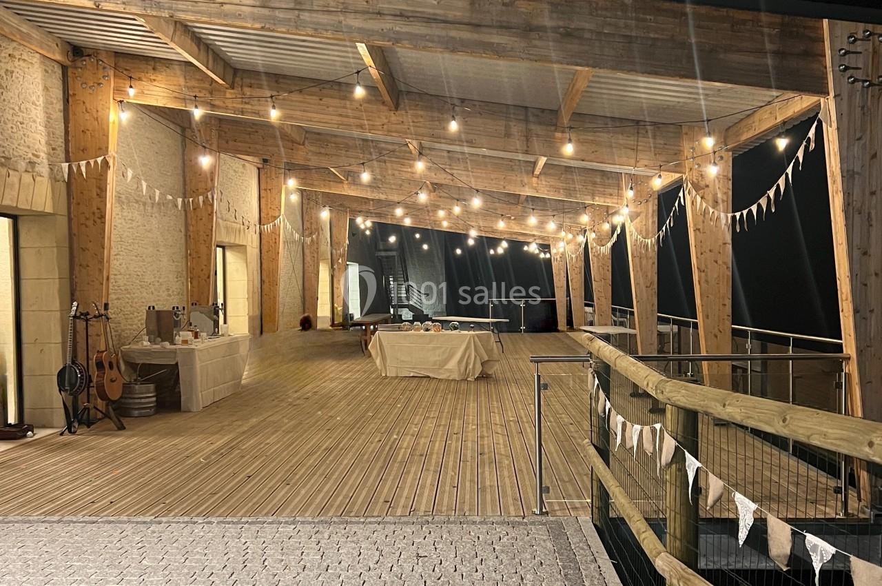 Terrasse en bois éclairée par des guirlandes lumineuses, décorée de fanions, avec des tables dressées en arrière-plan.