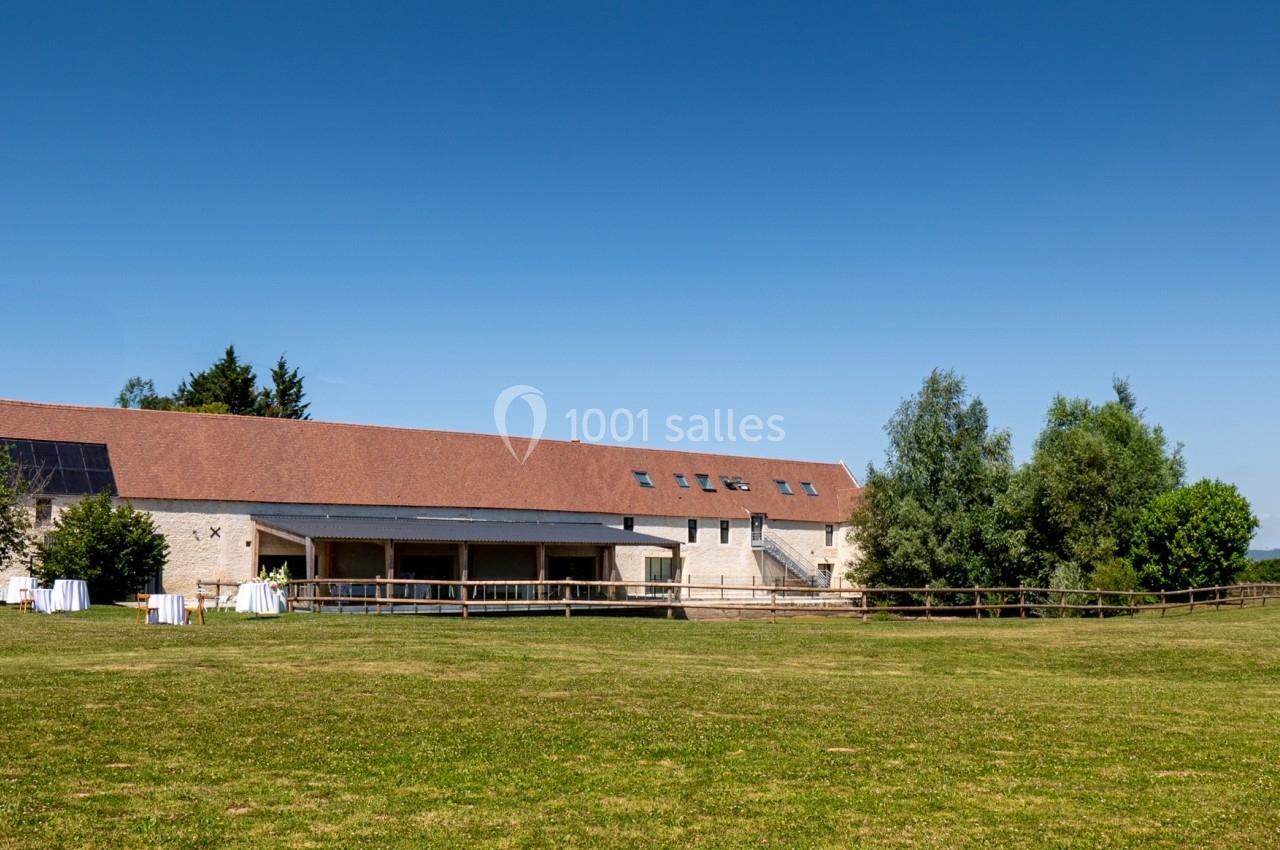 Bâtiment en pierre avec toit rouge entouré de verdure, sous un ciel bleu dégagé.