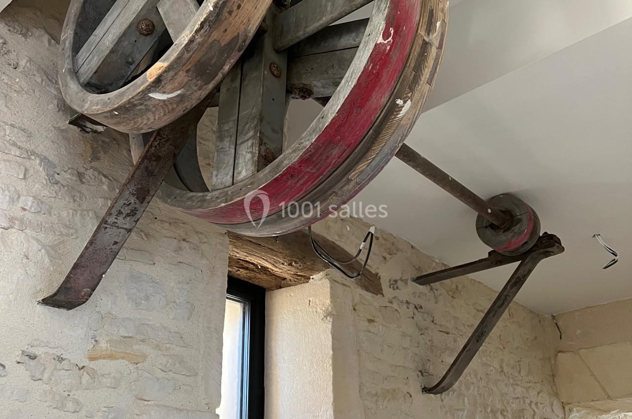 Mécanisme ancien avec roues en bois et métal fixé à un mur en pierre dans un intérieur lumineux.