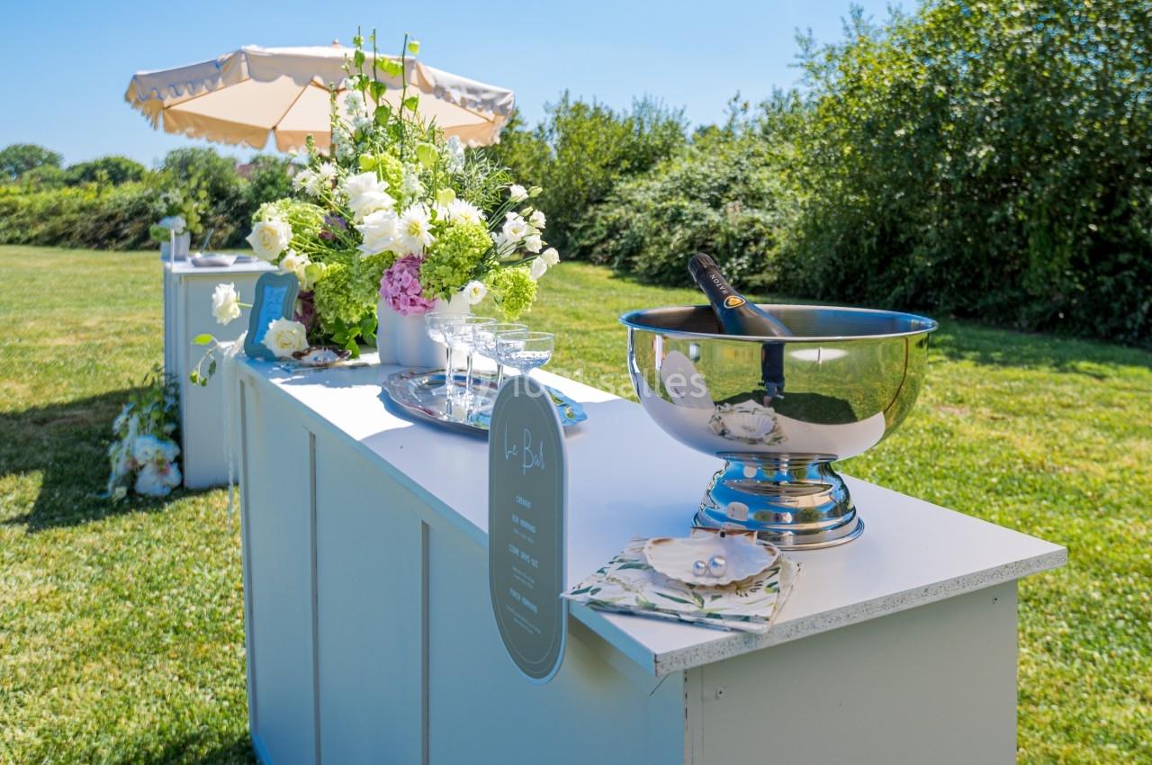 Table extérieure avec des fleurs, une vasque à champagne et des verres, installée dans un jardin ensoleillé.