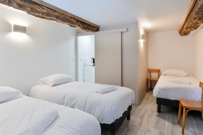 Chambre lumineuse sous les combles avec quatre lits simples, poutres apparentes et fenêtre de toit.