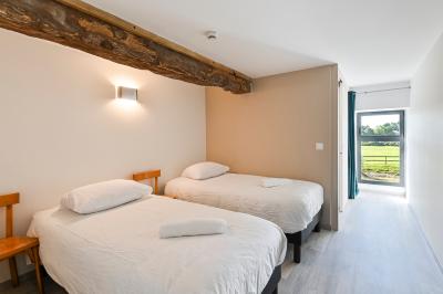 Chambre lumineuse sous les combles avec quatre lits simples, poutres apparentes et fenêtre de toit.