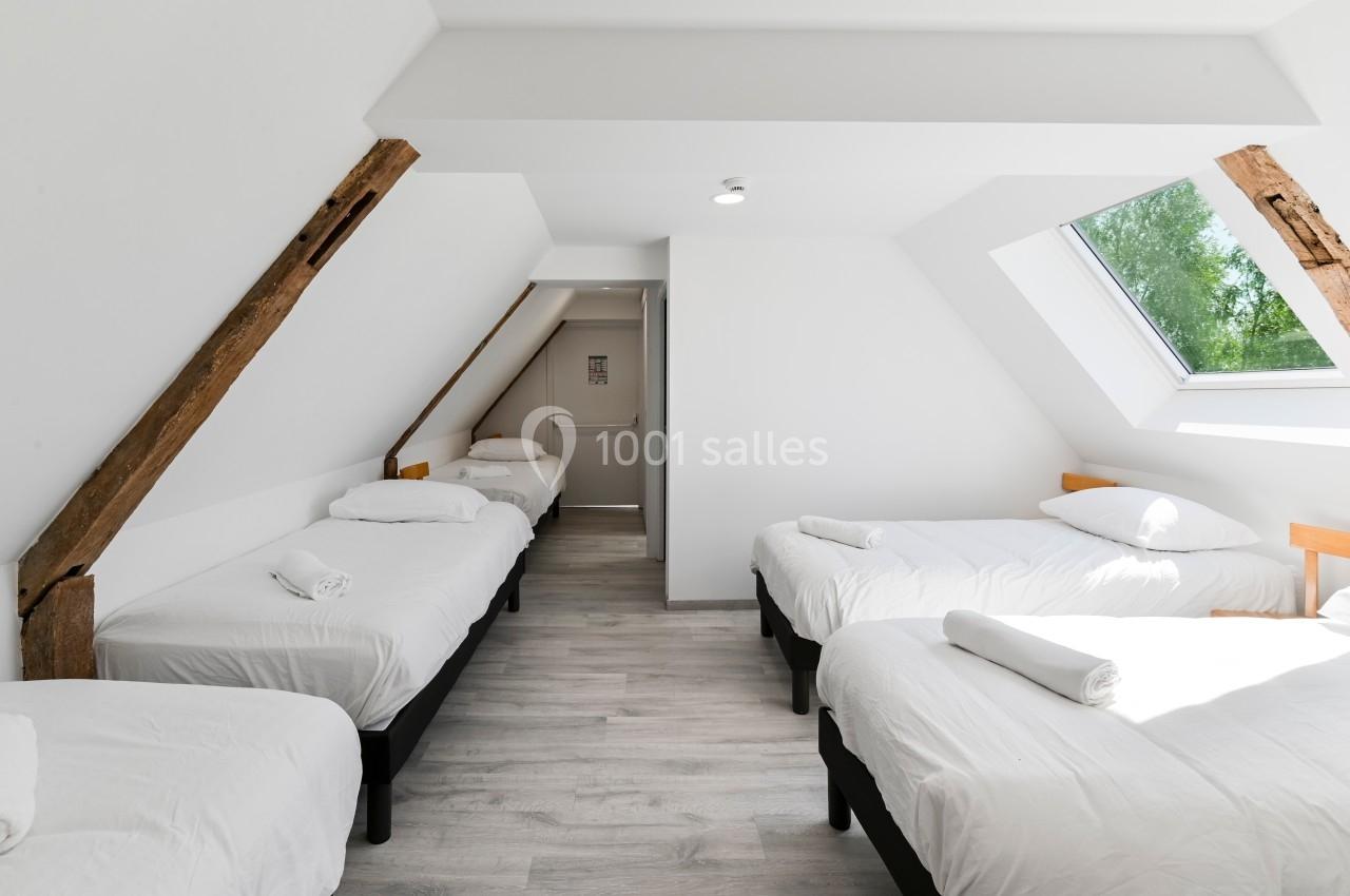 Chambre lumineuse sous les combles avec quatre lits simples, poutres apparentes et fenêtre de toit.