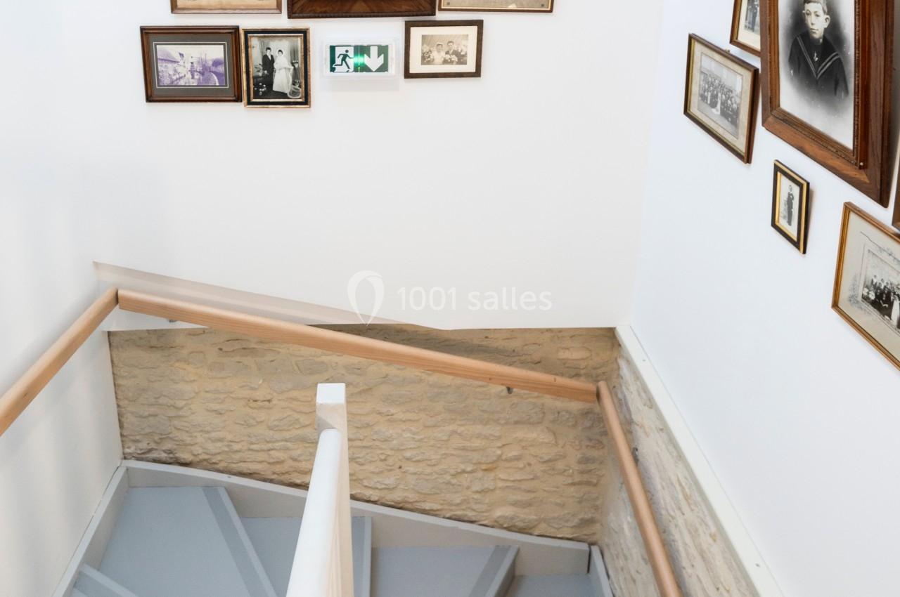 Escalier intérieur en bois peint en gris, entouré de murs ornés de cadres photo anciens.