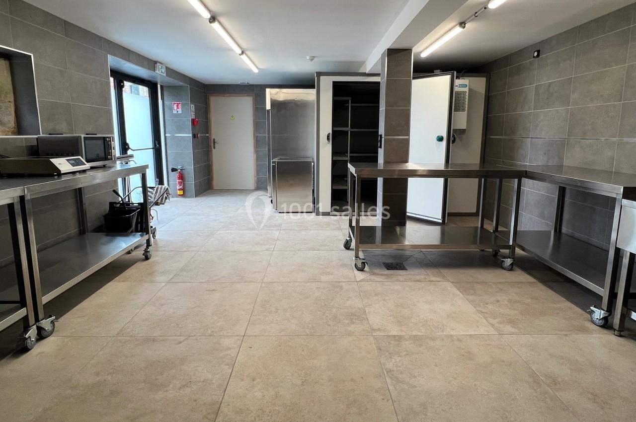 Cuisine professionnelle avec plans de travail en acier inoxydable, sol carrelé et équipements de stockage.