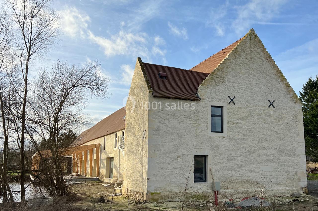 Bâtiment en pierre rénové avec toit en tuiles, entouré d'arbres et d'un ciel dégagé.
