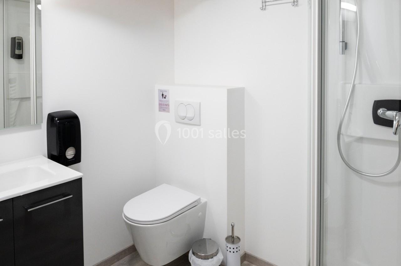 Salle de bain moderne avec douche arrondie, toilettes suspendues, lavabo noir et poutre apparente au plafond.