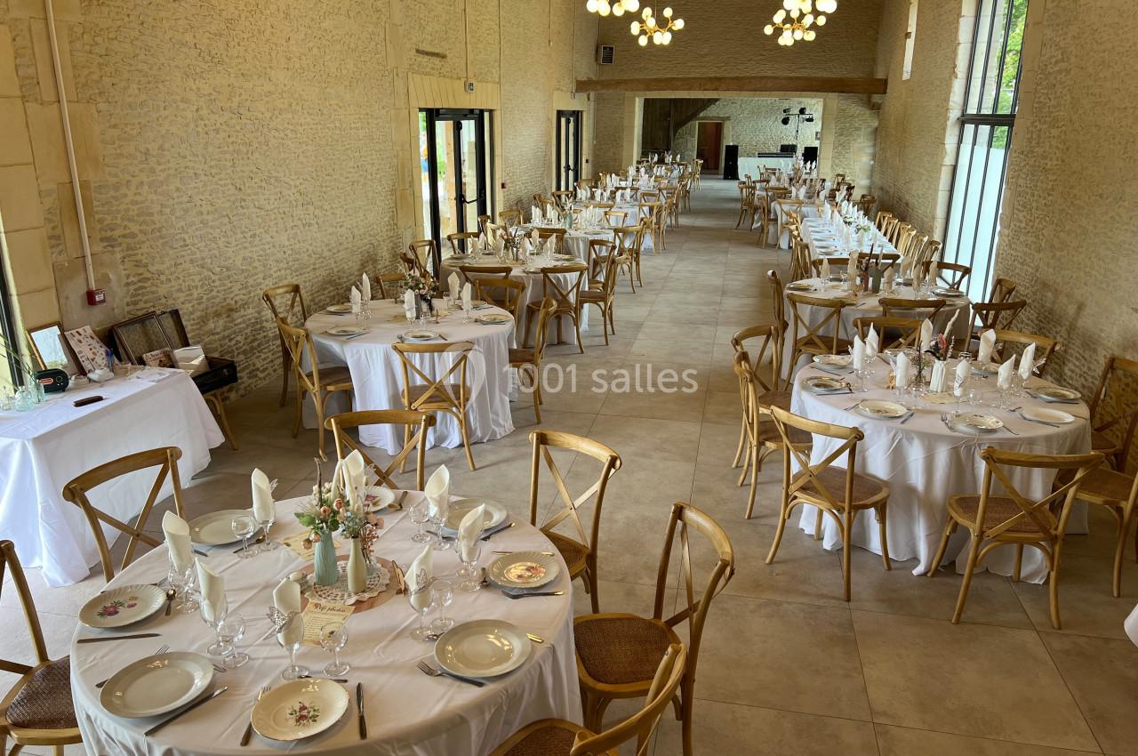 Salle de réception lumineuse avec tables rondes dressées, chaises en bois et décoration élégante.