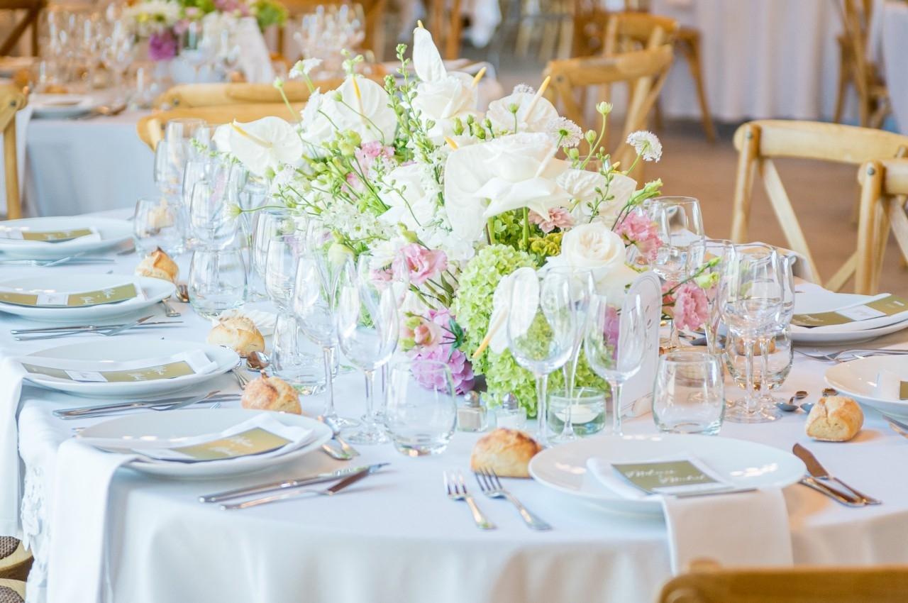 Table de réception élégamment dressée avec nappes blanches, vaisselle, verres et centre de table floral.