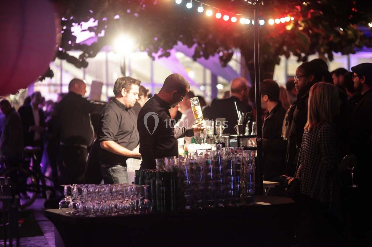 Des personnes rassemblées autour d'un bar en extérieur, éclairées par des lumières colorées dans une ambiance nocturne.