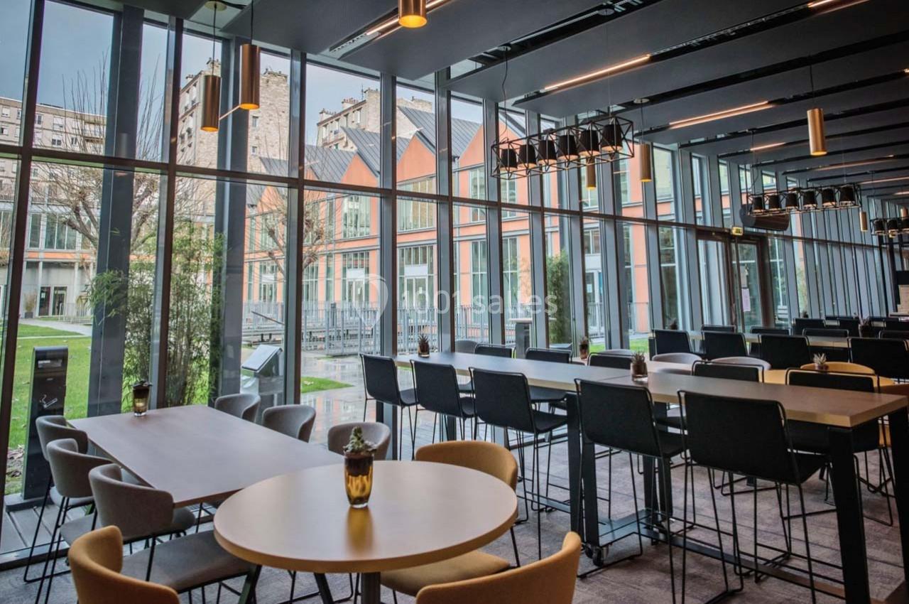 Salle lumineuse avec de grandes baies vitrées, mobilier moderne et vue sur un espace extérieur arboré.