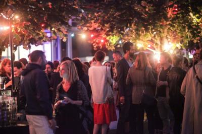 Un technicien supervise un enregistrement en studio, avec trois personnes chantant derrière une vitre insonorisée.