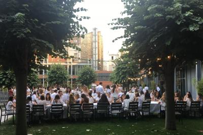 Un technicien supervise un enregistrement en studio, avec trois personnes chantant derrière une vitre insonorisée.