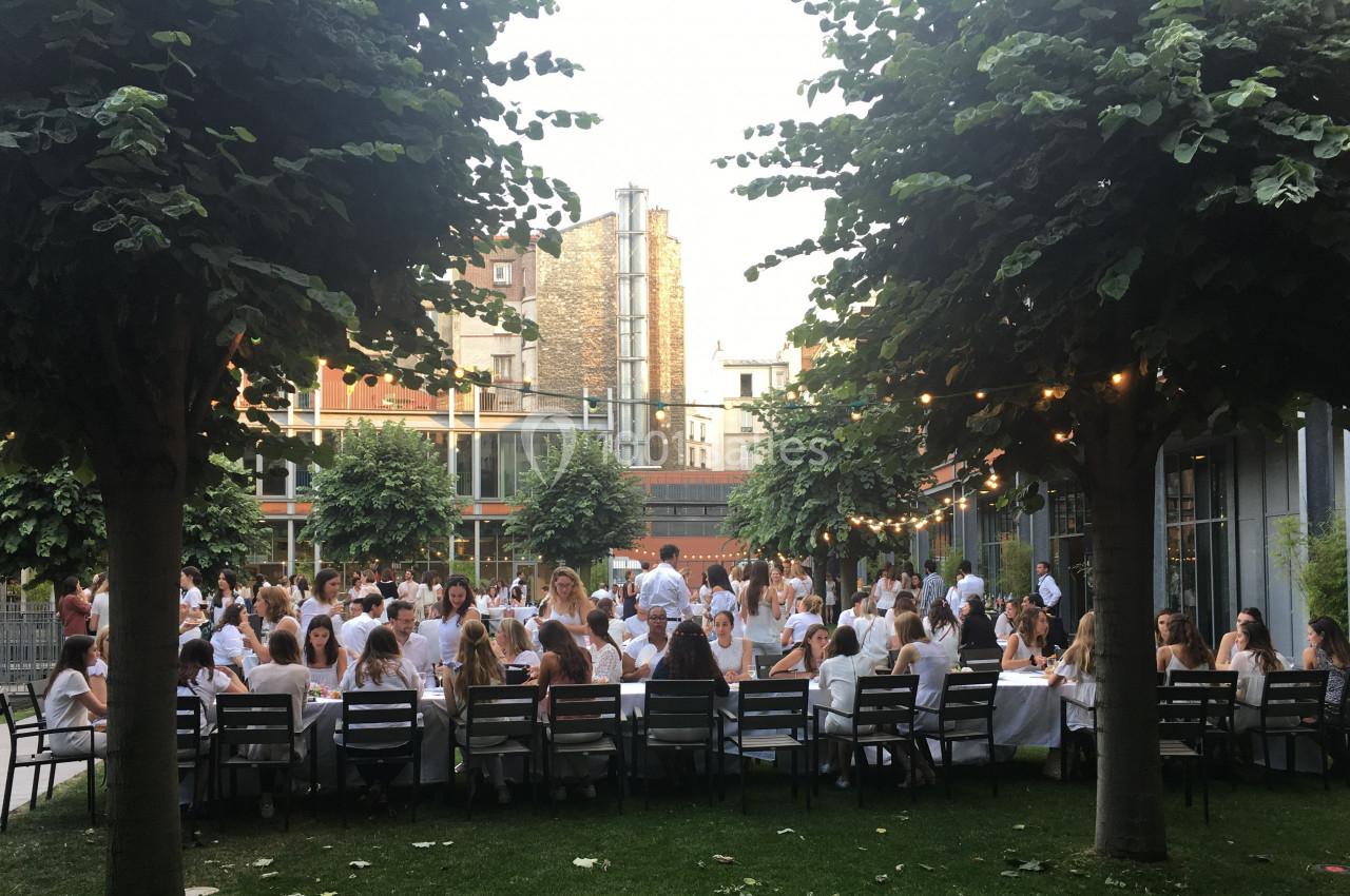 Groupe de personnes vêtues de blanc dînant à l'extérieur sous des arbres dans une ambiance conviviale.