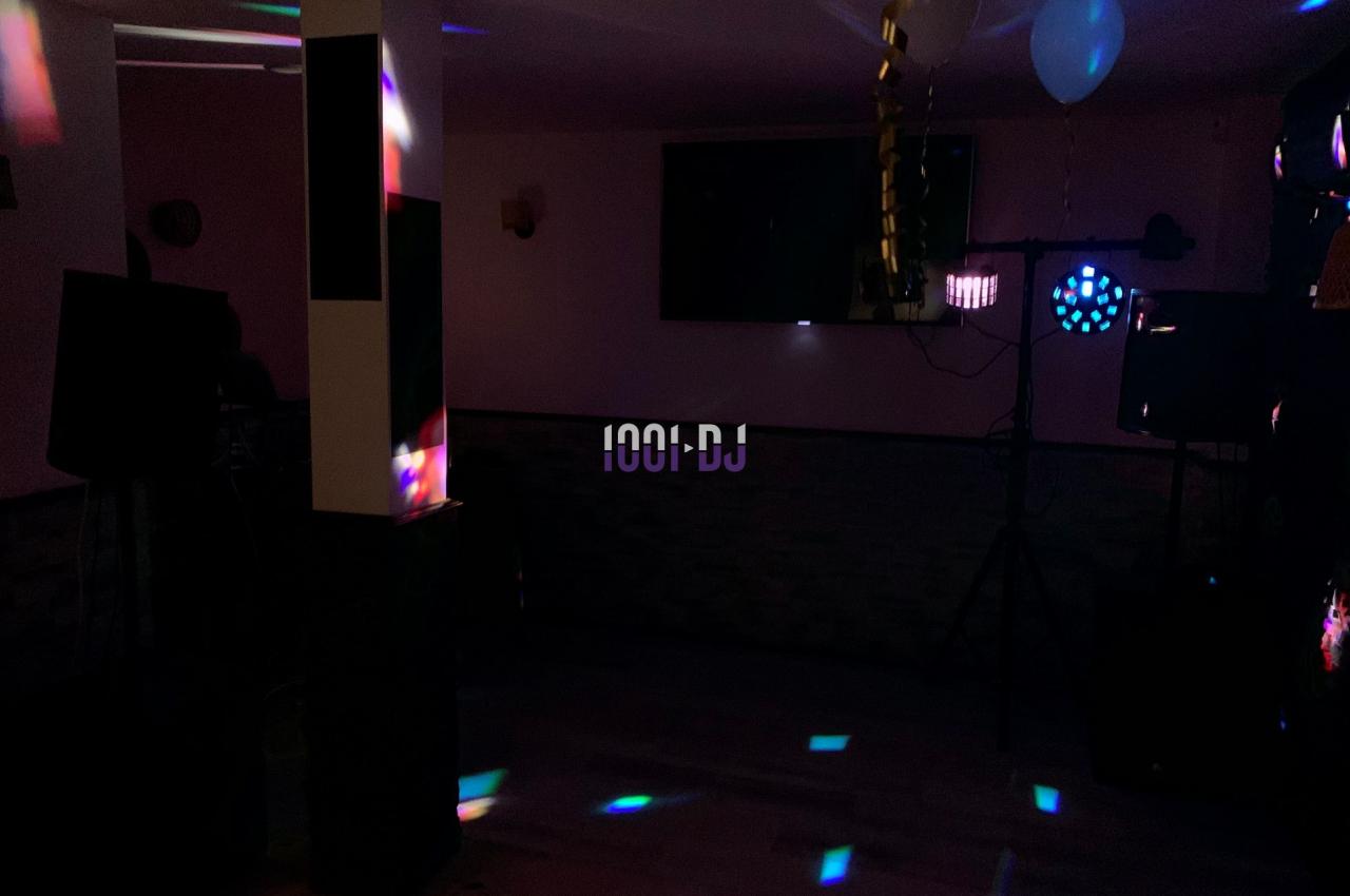 Salle sombre avec jeux de lumières colorées, décorée de ballons et guirlandes, équipée de matériel de sonorisation.