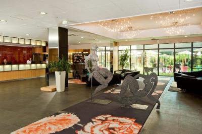 Salle de conférence avec des rangées de chaises grises et jaunes, une scène et une voiture en arrière-plan.